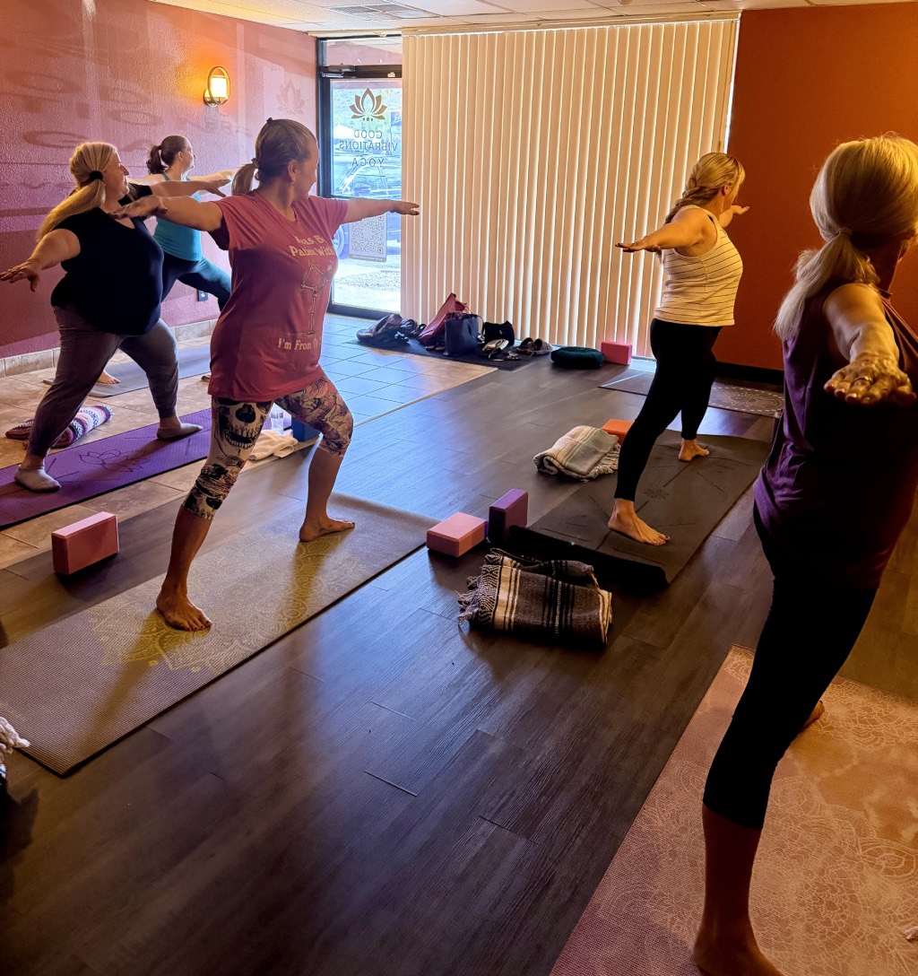 Students holding Warrior Two in a bright morning Basics class, arms stretched wide