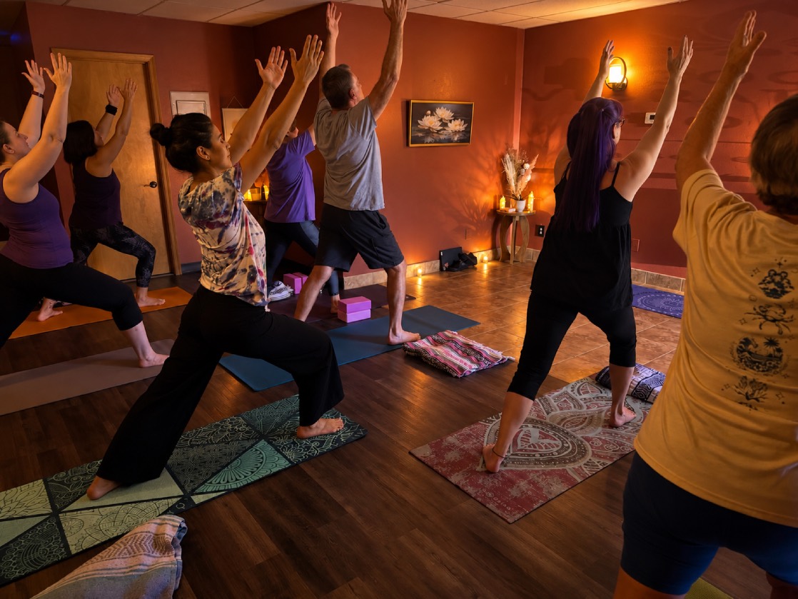 A full class reaching up into Warrior One on their mats in the candlelit studio at Good Vibrations Yoga